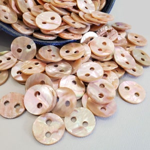 May include: A pile of iridescent pink and white shell buttons with two holes each. The buttons are round and have a smooth, polished finish.