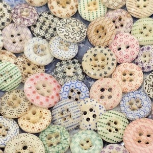 May include: A selection of decorative buttons in diverse colours and patterns. The buttons display designs like dots, stars, and swirls. Colours include white, pink, blue, green, and beige. Each button has four holes for sewing.