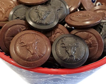 May include: A bowl filled with a variety of brown and black buttons featuring a deer head design. The buttons are made of a textured material and have a raised deer head design.