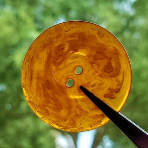 May include: A close-up of a yellow button with a marbled pattern. The button has two holes in the center.