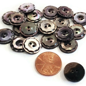 May include: A pile of 18 black and iridescent shell buttons with two holes each. The buttons have a scalloped edge and are approximately the size of a US penny.