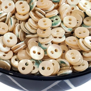 May include: A bowl filled with a large quantity of two-hole, white, mother-of-pearl buttons with green trim.