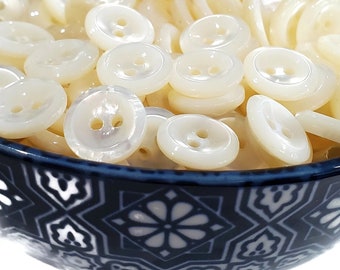 May include: A bowl filled with white mother of pearl buttons. The buttons have two holes and are arranged in a random pattern. The bowl is blue and white with a geometric design.