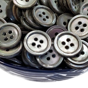May include: A bowl filled with a variety of iridescent black and grey shell buttons. The buttons have four holes each and are arranged in a random pattern.