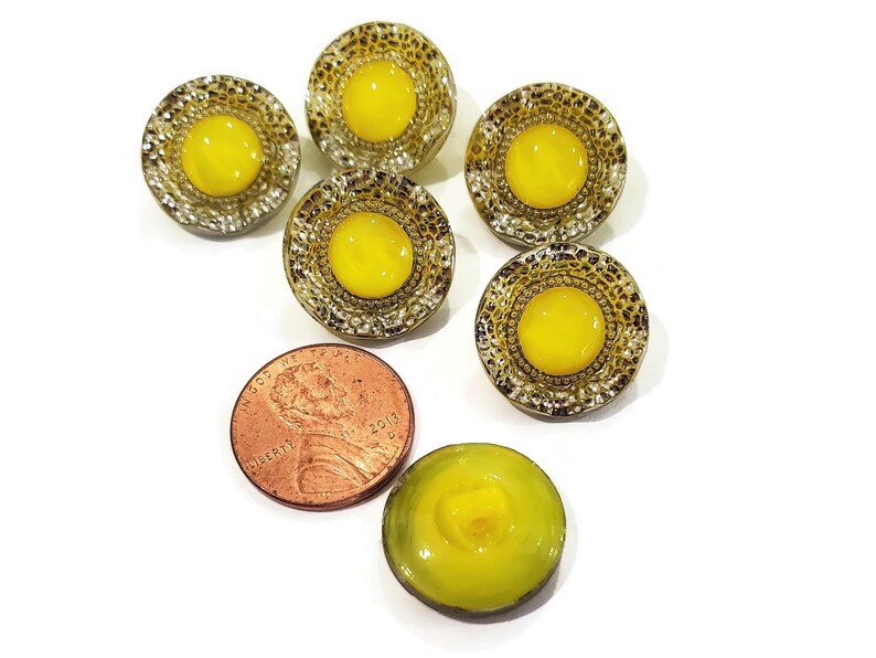 Back side of vintage moon glow glass buttons with the molded shank visible. The centers of the buttons are lemon yellow and the rims have a sparkly silver luster.