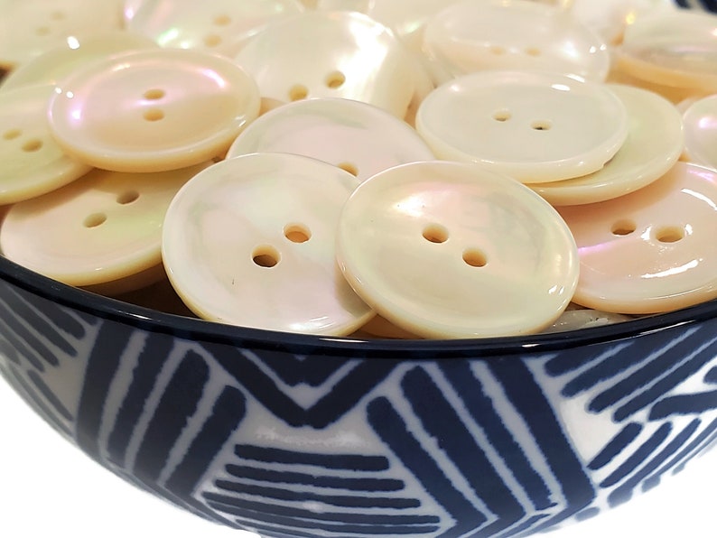 May include: A bowl filled with white iridescent buttons. The buttons have two holes and are arranged in a random pattern. The bowl is blue and white with a geometric design.
