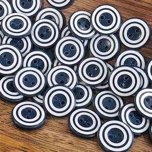 May include: A pile of navy blue and white striped buttons. Each button is round with two holes and concentric white stripes on a navy blue base. The buttons are scattered on a wooden surface.