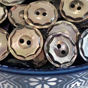 May include: A bowl filled with iridescent, dark brown, two-hole buttons. The buttons have a scalloped edge and a shiny finish.