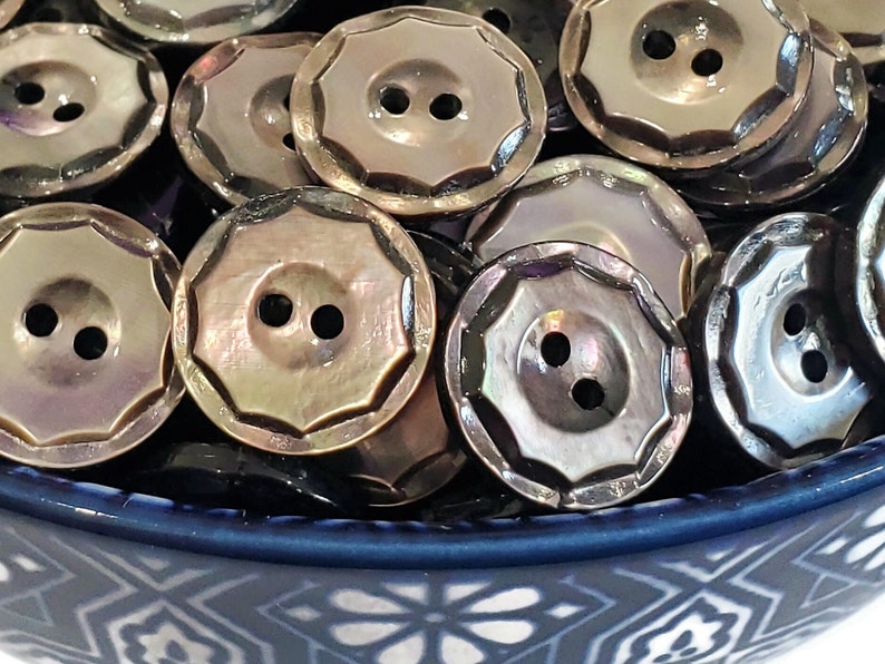May include: A bowl filled with iridescent, dark brown, two-hole buttons. The buttons have a scalloped edge and a shiny finish.