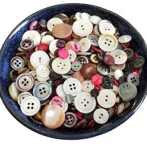 May include: A bowl filled with a variety of colorful buttons in different shapes and sizes. The buttons are made of various materials, including plastic, metal, and wood. Some of the buttons have a pearl-like finish.