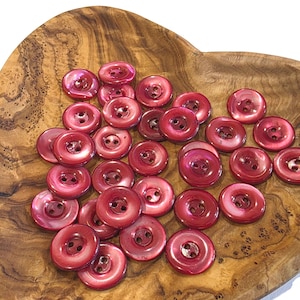 May include: A collection of round, two-hole buttons in a deep, glossy burgundy red finish. Each button features a smooth, slightly concave center and a raised outer rim, showcasing a consistent, reflective surface texture across the entire set.