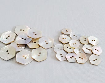 May include: A collection of white iridescent mother of pearl buttons with two holes each. The buttons are hexagonal in shape.