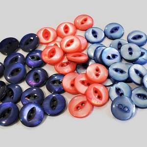 May include: A collection of blue and red two-hole buttons with a pearlescent finish. The buttons are arranged in a semi-circle pattern.