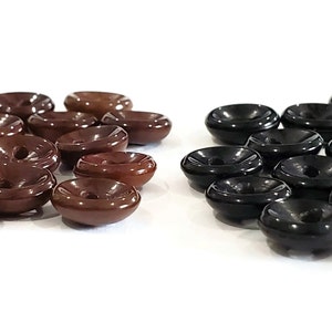 May include: A collection of dark brown and black wooden buttons. The buttons have a shallow bowl shape with a central hole. The buttons are arranged in two groups against a white background.