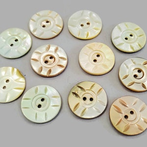 May include: A collection of twelve iridescent mother-of-pearl buttons with two holes each. The buttons have a variety of designs, including sunburst and floral patterns.