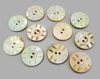 May include: A collection of twelve iridescent mother-of-pearl buttons with two holes each. The buttons have a variety of designs, including sunburst and floral patterns.
