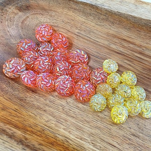 May include: A collection of small, round, translucent buttons featuring a textured, faceted surface that reflects light. The set includes a group of vibrant orange buttons and a separate cluster of bright yellow buttons, all with a shimmering finish.
