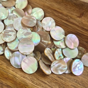 May include: A selection of iridescent, round mother-of-pearl shell beads. The beads are in shades of white, pink, and green. They are arranged in a wooden bowl, creating a natural and elegant aesthetic. Suitable for jewellery making and crafts.