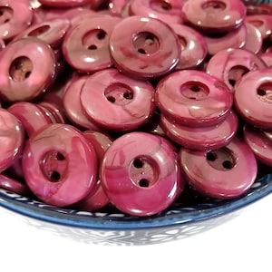 May include: A bowl filled with a large quantity of two-hole, round, burgundy-colored buttons. The buttons have a shiny, iridescent finish.