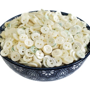 May include: A bowl filled with white and green iridescent buttons. The buttons are round and have two holes.