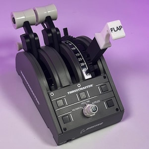 Könnte beinhalten: Ein graues und schwarzes Thrustmaster-Flugsimulator-Bedienfeld mit zwei weißen Schubhebeln, einem Klappenhebel und einem Knopf mit der Aufschrift "SEL". Das Bedienfeld hat Beschriftungen für "HDG/TRK", "JAS/MACH" und "ALTITUDE". Das Bedienfeld trägt auch das Boeing-Logo.