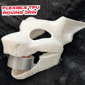 May include: A white, 3D-printed skull mask with a flexible moving jaw, held open with grey tape. The mask has a textured surface and the text "FLEXIBLE TPU MOVING JAW" in red and white.