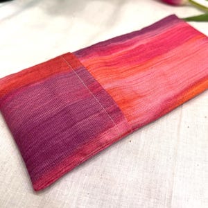 Puede incluir: Una almohada rectangular para los ojos en tonos de rojo, rosa y morado. La tela tiene un aspecto texturizado y est&aacute; dividida en dos secciones, con una costura visible. La almohada est&aacute; dise&ntilde;ada para la relajaci&oacute;n y la aromaterapia.