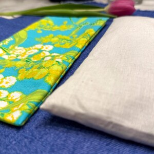 Puede incluir: Primer plano de dos art&iacute;culos de tela. Uno es una tela rectangular turquesa con un estampado floral en amarillo y blanco. El otro es una tela rectangular blanca. Ambos est&aacute;n sobre una superficie azul.