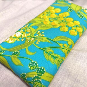 Puede incluir: Un art&iacute;culo de tela rectangular con un vibrante estampado floral. El dise&ntilde;o presenta flores y hojas amarillas, verdes y blancas sobre un fondo turquesa brillante. La tela est&aacute; doblada, lo que sugiere que podr&iacute;a ser una funda o cubierta.