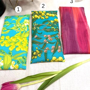 Puede incluir: Tres bolsas rectangulares de tela con estampados florales. Dos bolsas tienen un fondo turquesa con dise&ntilde;os florales amarillos y verdes. La tercera bolsa tiene un estampado tie-dye rosa y morado. Un tulip&aacute;n rosa y hojas verdes en primer plano.