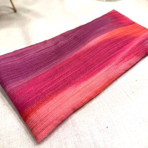 Puede incluir: Un textil rectangular con un degradado de colores, que transita del morado intenso al rosa vibrante y coral. La tela tiene una apariencia texturizada, con l&iacute;neas horizontales visibles. La est&eacute;tica general es suave y colorida.