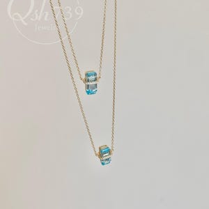 May include: Two gold necklaces with a pendant featuring a rectangular, light blue gemstone. The gemstone is accented with small, clear stones. The necklaces are displayed against a white background. The text "Qsh739 Jewelry" is in the upper left corner.