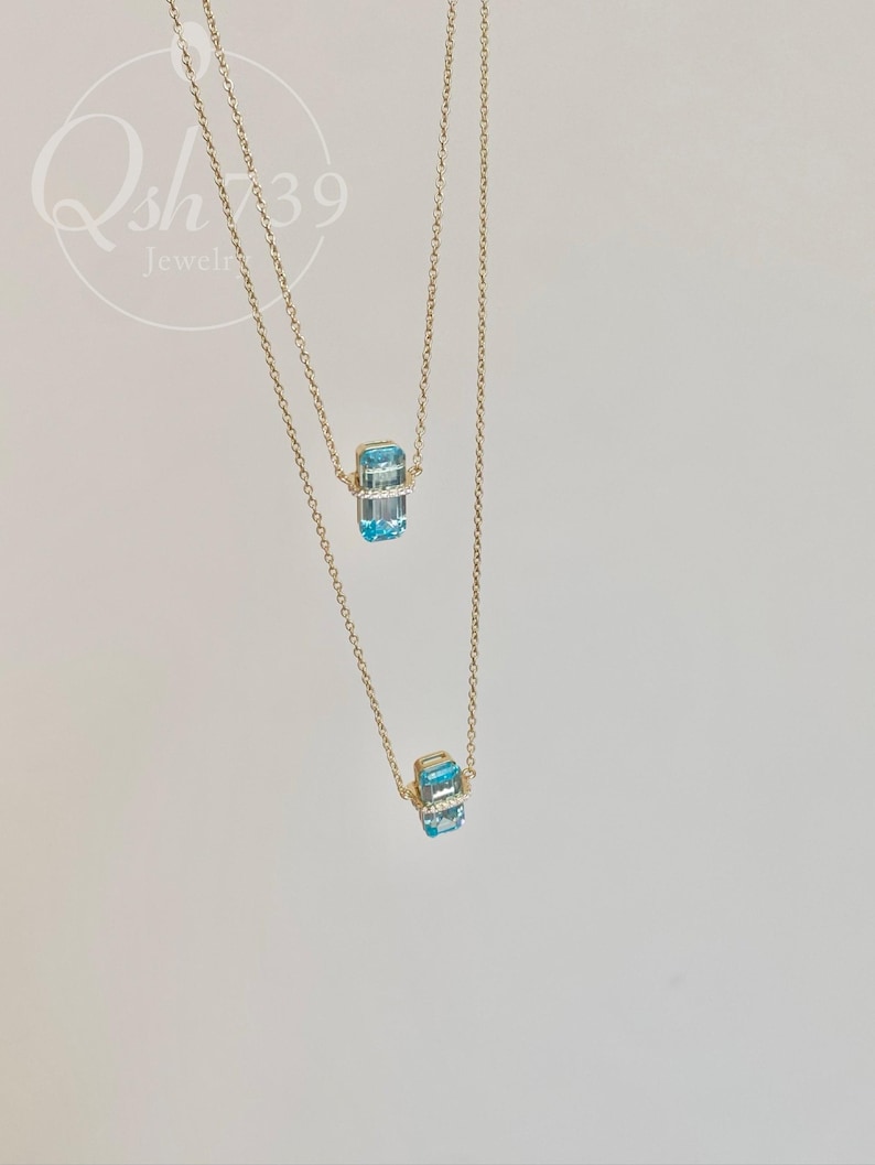 May include: Two gold necklaces with a pendant featuring a rectangular, light blue gemstone. The gemstone is accented with small, clear stones. The necklaces are displayed against a white background. The text "Qsh739 Jewelry" is in the upper left corner.
