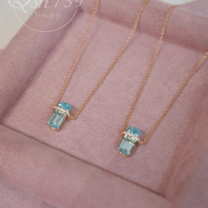 May include: Two gold necklaces with rectangular, light blue gemstone pendants. Each pendant is accented with small, clear stones. The necklaces are displayed on a pink surface. The jewelry is from Qsh739 jewelry.