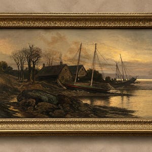 May include: An oil painting in a decorative gold frame depicting a coastal scene at sunset. The landscape features two small houses near the water, bare trees on a rocky shoreline, and two sailboats moored along the bank under a golden sky.