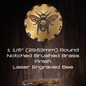 May include: A round, notched brass cabinet knob with a brushed finish. The knob features a laser-engraved bee design. The text on the image reads: 1 1/16" (29.63mm) Round Notched Brushed Brass Finish Laser Engraved Bee.