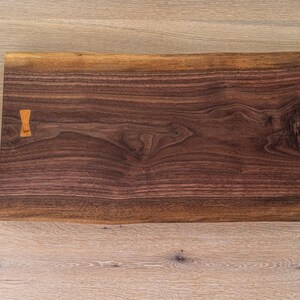 May include: A large, rectangular wooden cutting board made of walnut with a natural edge. The board has a small wooden handle on one side.
