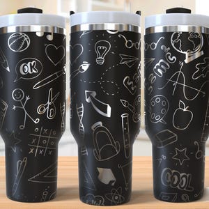 Könnte beinhalten: Drei schwarze Reisebecher mit weißen Deckeln und Griffen, verziert mit silbernen Kritzeleien von schulbezogenen Gegenständen. Die Becher stehen auf einer Holzoberfläche. Jeder Becher hat ein Fassungsvermögen von ca. 470 ml.