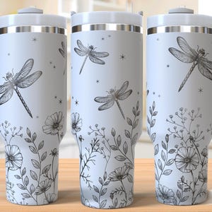 May include: A white stainless steel travel mug with a black and white dragonfly and floral design. The mug has a handle and a lid.