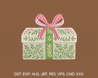 Op de afbeelding: Geborduurde geschenkdoos met een roze strik en groen bladerontwerp. De doos is wit met groene bladeren en een groene verticale streep. De achtergrond is bruin. Tekst onderaan: DST, EXP, HUS, JEF, PES, VP3, CND, XXX.