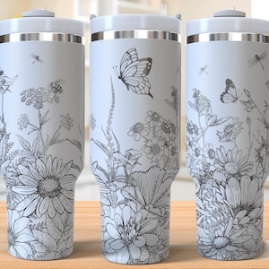 May include: Three white stainless steel tumblers with a black and white floral design featuring butterflies and dragonflies. The tumblers have a silver lid and a handle.
