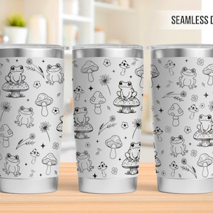 May include: Three white stainless steel tumblers with a black and white seamless design featuring frogs sitting on mushrooms, flowers, and stars.  The design is repeated on all three tumblers.