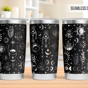 Pode incluir: Três copos de aço inoxidável com fundo preto e um padrão prateado de luas, estrelas, cristais e outros símbolos celestiais. Os copos estão dispostos em fila, com o copo do meio ligeiramente mais alto que os outros. O texto "SEAMLESS DESIGN" é visível no canto superior direito da imagem.