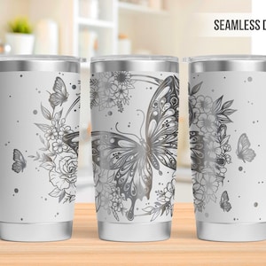 May include: White stainless steel tumbler with a wraparound design featuring butterflies and floral elements in shades of gray. The tumbler has a silver rim and base. The words "SEAMLESS DESIGN" are printed at the top.