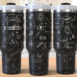 Puede incluir: Tres tazas de viaje de acero inoxidable negro con un diseño blanco de herramientas de costura y una regla. El diseño incluye una máquina de coser, tijeras, botones, agujas, hilo y una cinta métrica. Las tazas tienen una tapa blanca y un asa negra.