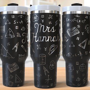 May include: Black insulated travel mug with a white lid and handle. The mug is decorated with silver-colored math symbols and the name "Mrs. Hannah" in a script font. The design includes geometric shapes and equations.
