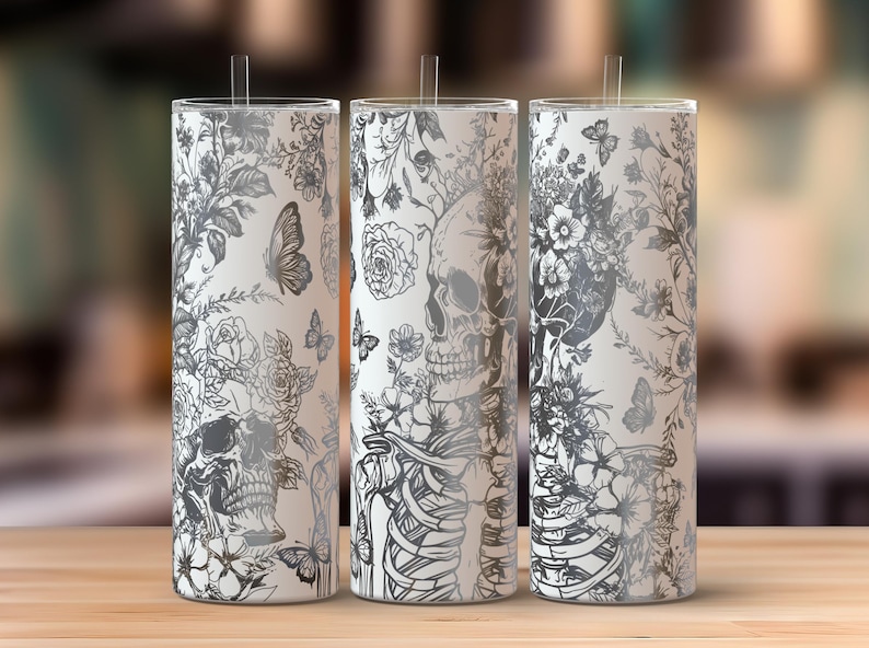 K&ouml;nnte beinhalten: Drei wei&szlig;e Edelstahlbecher mit einem schwarz-wei&szlig;en Blumen- und Sch&auml;delmuster. Die Becher haben ein Strohloch und einen Deckel.