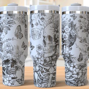 May include: Three white stainless steel tumblers with a black and white floral design featuring a skull and skeleton. The tumblers have a handle and are approximately 568 ml in size.