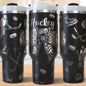 May include: Black stainless steel tumbler with a hockey mum design. The tumbler features a leopard print bow, hockey sticks, and a hockey puck. The text "Hockey Mum" is printed on the tumbler.