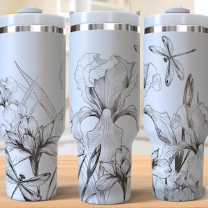 May include: White travel mug with a floral and dragonfly design. The mug features a detailed black and white illustration of irises and dragonflies. The mug has a white lid and handle, and the words "SEAMLESS DESIGN" are printed on the side.